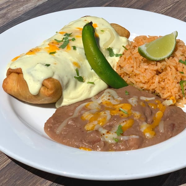 Serrano's Mexican Food chimichanga covered in white sauce, with rice, beans, and a lime wedge.