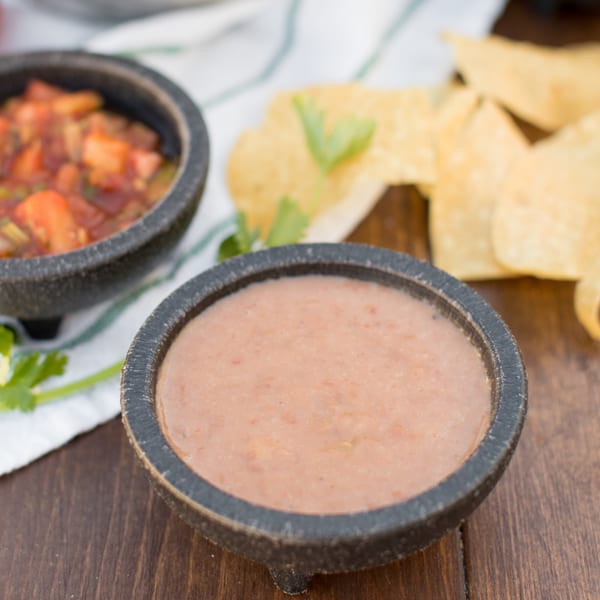 Two bowls of Serrano's Mexican dips, one with refried beans and another with salsa, alongside tortilla chips.