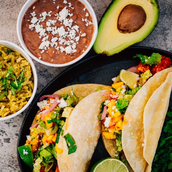 Serrano's Mexican Food tacos with rice, beans, and avocado on a dark plate.