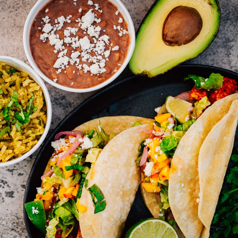 Serrano's Mexican Food tacos with rice, beans, and avocado on a dark plate.