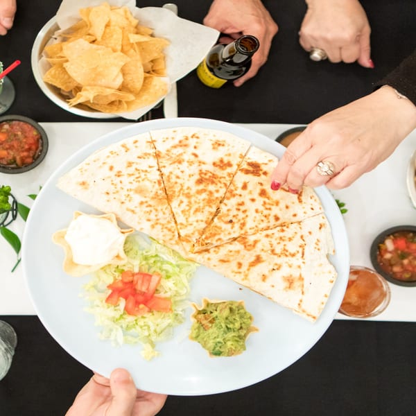 A Serrano's quesadilla with guacamole, sour cream, and lettuce, served with chips and salsa.