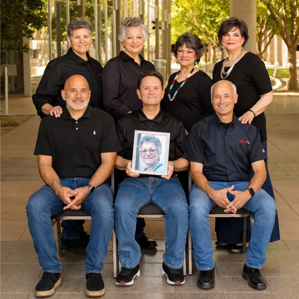 Six adults, three men seated and three women standing behind, with one man holding a framed photo.