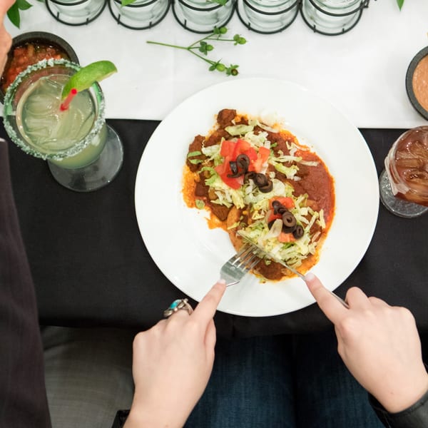 Overhead view of a person cutting into a plate of Mexican food with a margarita.
