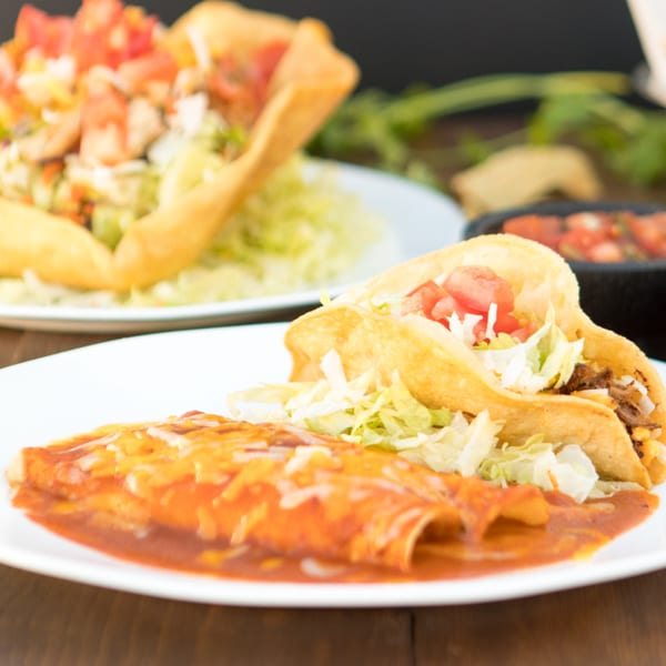 A plate of Serrano's Mexican food with two tacos and two enchiladas, topped with lettuce, tomatoes, and cheese.