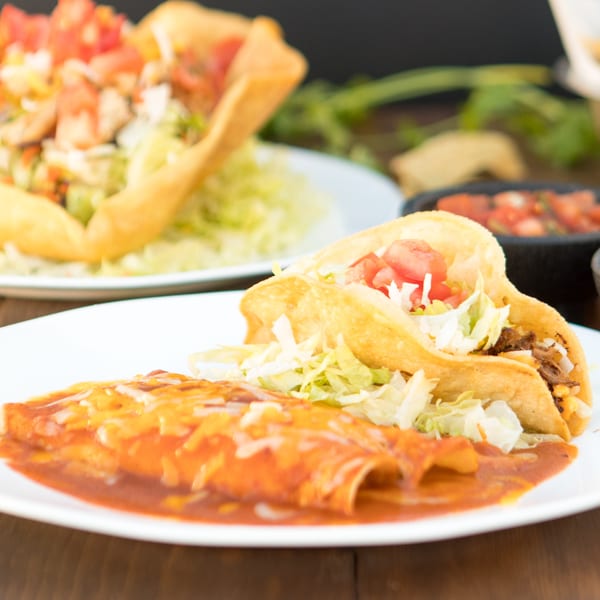 Serrano's Mexican Food: Two crispy tacos and enchiladas with red sauce and melted cheese.