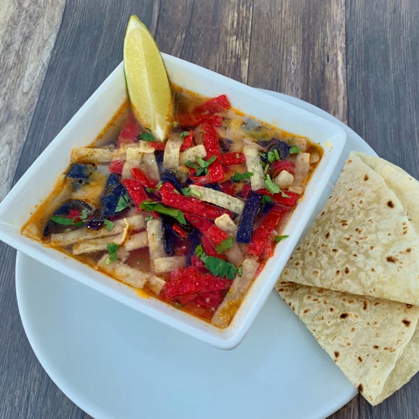 Serrano's Mexican tortilla soup with red, white, and blue tortilla strips, cilantro, and a lime wedge.