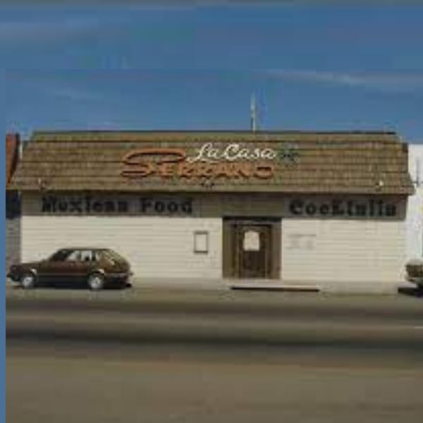 Exterior of Serrano's Mexican restaurant with "La Casa Serrano Mexican Food Cocktails" sign and a car parked.