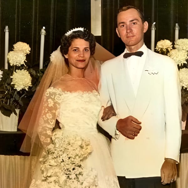 A vintage wedding photo of a bride in a white lace dress and a groom in a white tuxedo.