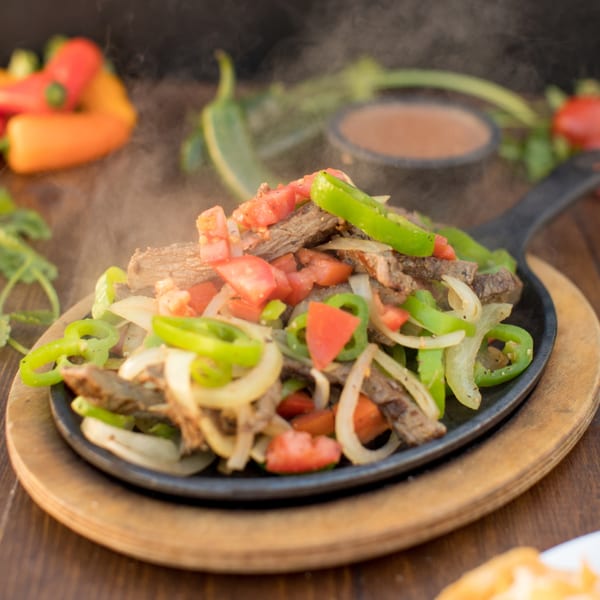 Sizzling Serrano's Mexican beef fajitas with bell peppers, onions, and tomatoes in a cast iron skillet.
