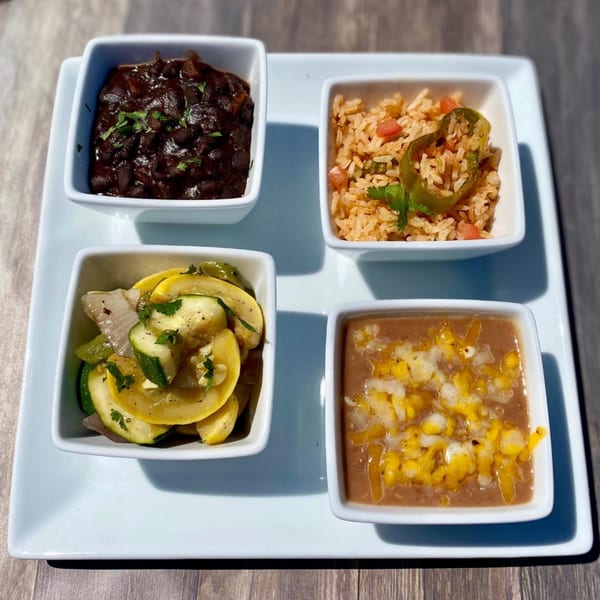 Four square bowls of Mexican side dishes: black beans, rice, sautéed squash, and refried beans with cheese.