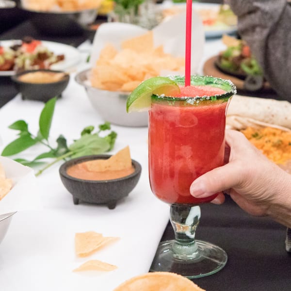 A hand holds a vibrant red strawberry margarita with a lime wedge and salted rim at Serrano's.
